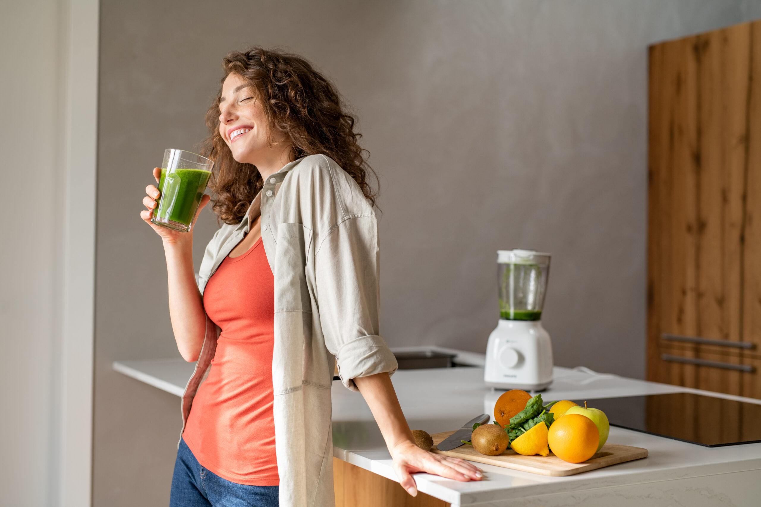 Happy,Young,Woman,Standing,In,Kitchen,And,Holding,Glass,Of